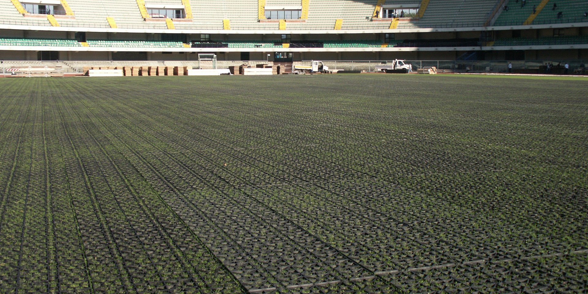 Kunststoffrasengitter auf dem Boden eines grossen Stadions mit grüner Wiese und leeren Sitzplätzen.