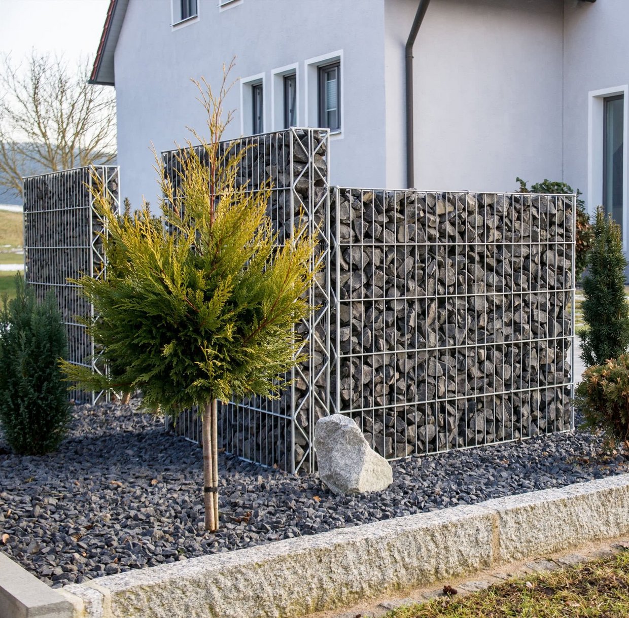 Zaunsteinkörbe bieten Sichtschutz im Garten eines Einfamilienhauses.